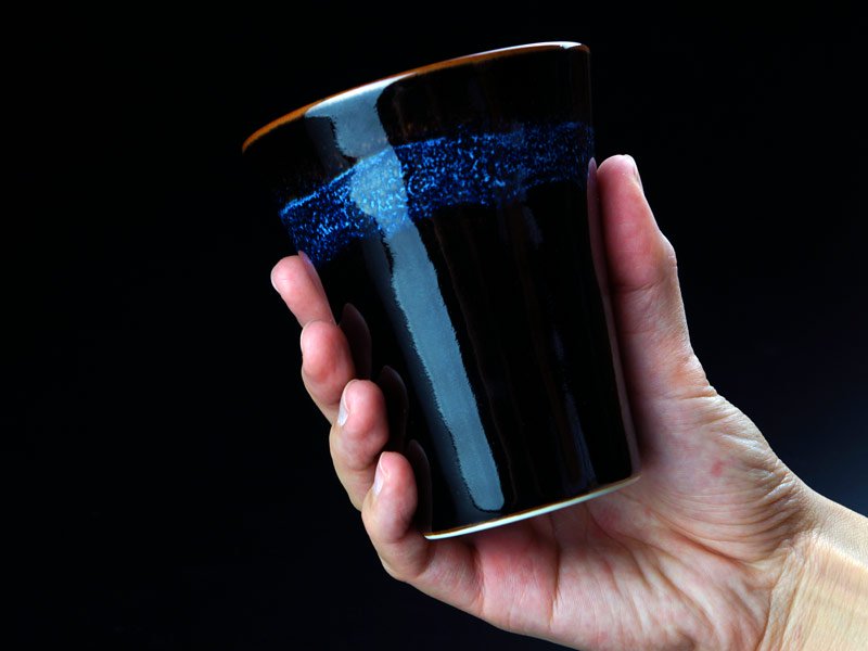 有田焼 焼酎グラス 青き明星。青い結晶の浮いた黒い焼酎グラスを手に持ったところ
